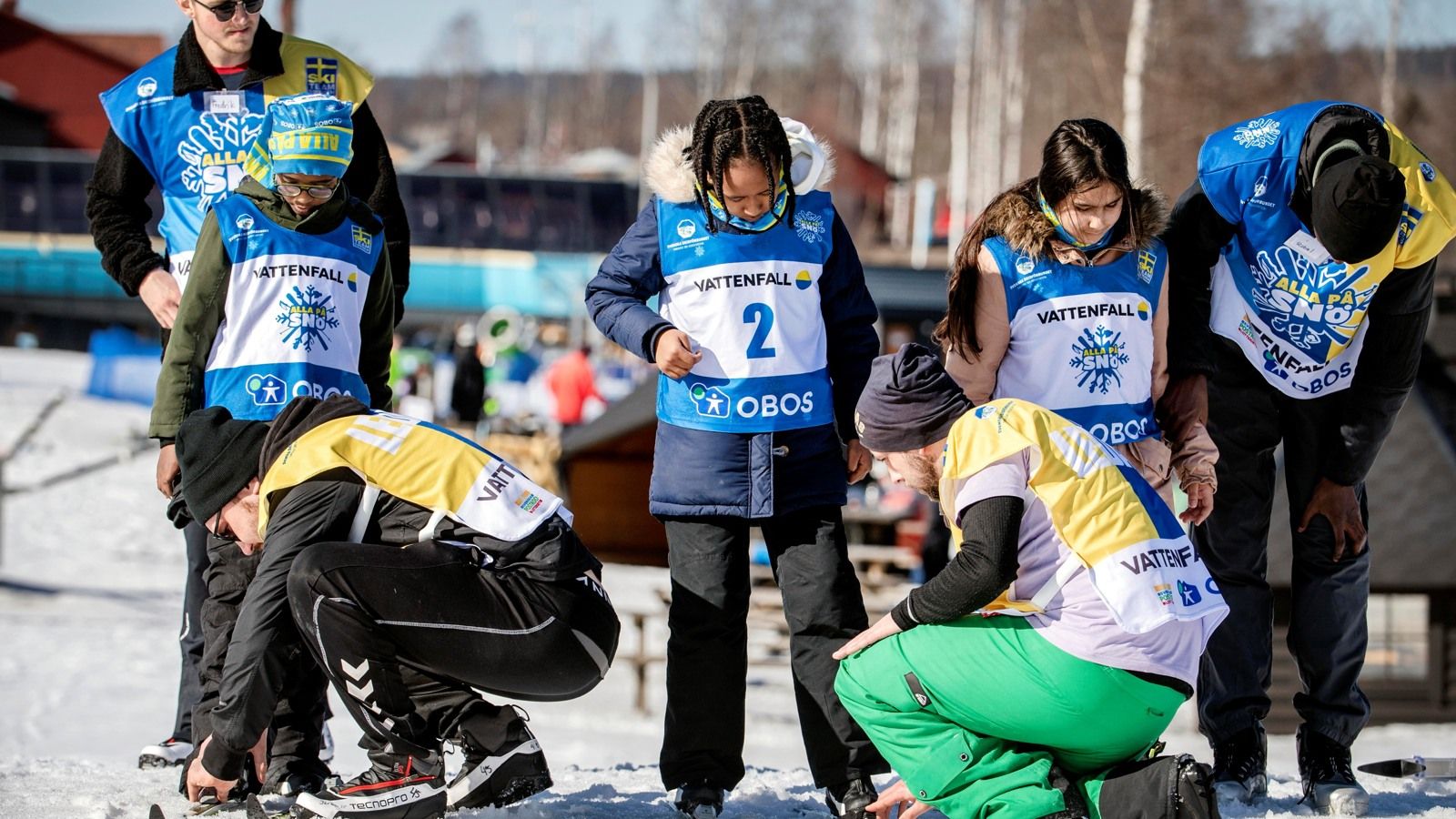 Två personer hjälper barn med deras skidor.