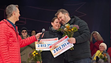 Rickard intervjuar ett par på scen, de håller i två checkar och blommor.
